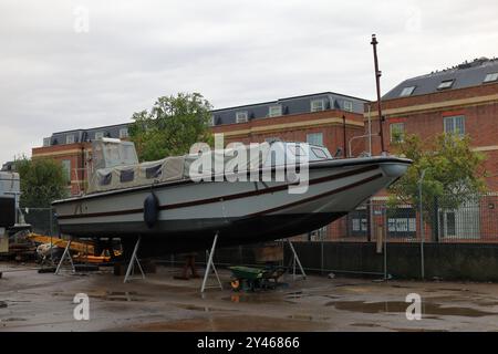 Gosport, Hampshire, England. 7. September 2024. Ein Boot wird an einem nassen Tag an Land neben Backsteinbauten repariert. Dieses Foto ist eines einer Serie, die ich an einem regnerischen Tag während einer kürzlich geführten Tour durch den Royal Clarence Victualing Yard während der Gosport Heritage Open Days gemacht habe. Stockfoto