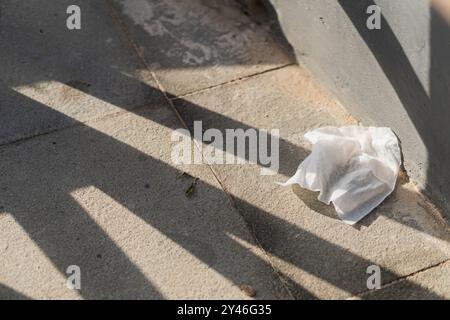 Ein zerknittertes Stück Papier, das auf einer strukturierten Betonoberfläche liegt, mit langen Schatten, die von einer benachbarten Struktur geworfen werden. Die Szene fängt einen Moment des urbanen Negativs ein Stockfoto