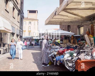 Cremona, Italien 31. August 2024 Eine Frau wählt auf einem Textilmarkt im Freien einen Stoff von einem Standhalter in italien Stockfoto