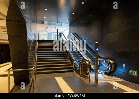 Abbildung: Treppe und Rolltreppe, die nach oben führen. Die Rolltreppe ist beleuchtet und an der Wand befindet sich ein Schild. Stockfoto