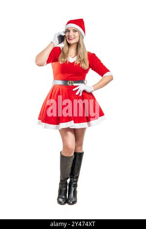 Junge lateinfrau verkleidet als weihnachtsmann, die an weihnachten auf dem Handy spricht und Hände auf weißem Hintergrund hält Stockfoto