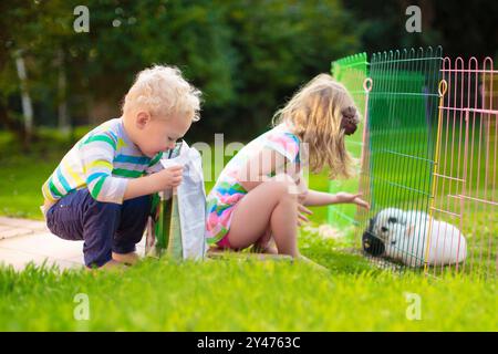 Kinder füttern Kaninchen im sonnigen Garten. Kinder, die flauschige Häschen füttern. Kind und Haustier und zu Hause. Tierfreundschaft und Tierpflege. Osterhasen. Stockfoto