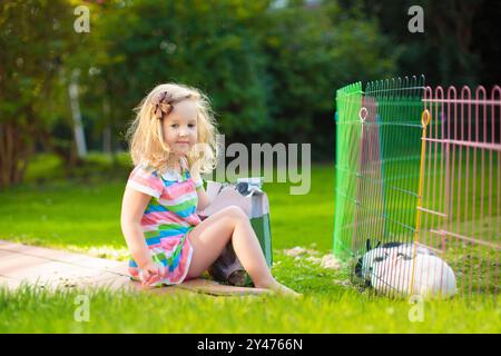 Kinder füttern Kaninchen im sonnigen Garten. Kinder, die flauschige Häschen füttern. Kind und Haustier und zu Hause. Tierfreundschaft und Tierpflege. Osterhasen. Stockfoto