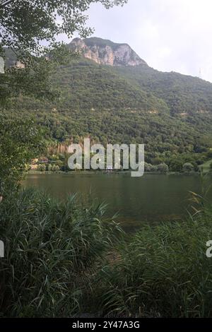 Bergsee bei Sonnenuntergang mit einem Dorf und einem Nebenfluss in einem Park, der von Bäumen und Schilf eingerahmt ist Stockfoto