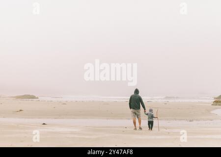 Ein Vater und ein Sohn, der am Strand in Richtung Meer läuft. Stockfoto