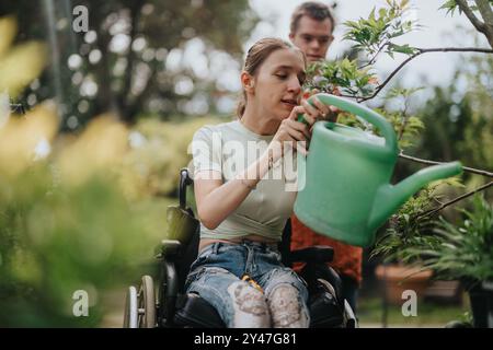 Junge Frau im Rollstuhl, die Pflanzen im Garten bewässert Stockfoto