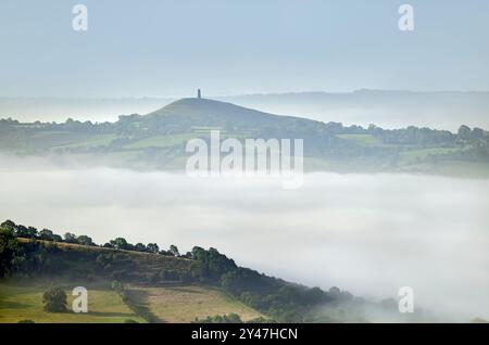 Starker Morgennebel auf den Somerset Levels, von den Mendip Hills, Somerset, Großbritannien mit sonnendurchflutetem Feld in den Vorgrouns und Glastonbury Tor in t Stockfoto