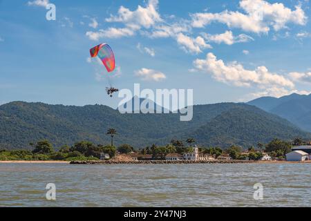 Paramotor fliegt am blauen Himmel von Paraty, Brasilien. Die Kirche unserer Schmerzensmutter vom Meer aus gesehen. Die Kolonialstadt wurde 1667 gegründet. Stockfoto