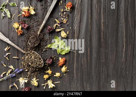 Zusammensetzung von trockenem schwarzem und grünem Tee in Vintage-Löffeln, trockenem Blumen Tee auf einem dunklen hölzernen Hintergrund von oben mit Platz für Text Stockfoto