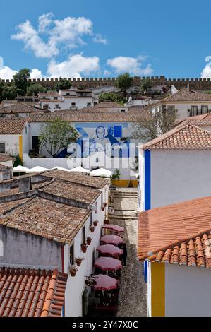 Farbenfrohe Wandgemälde und Terrakottadächer unter den mittelalterlichen Mauern in der historischen Stadt Óbidos Stockfoto