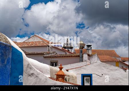 Dächer mit traditionellen Terrakottafliesen und verzierten Details unter dramatischen Wolken in Óbidos Stockfoto