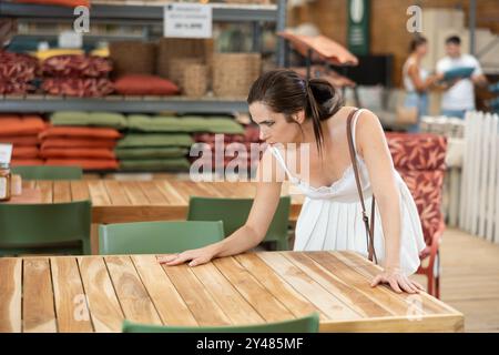 Hübsches Brünette Mädchen in weißem Kleid wählt Holztisch für Landhaus im Gartenladen Stockfoto