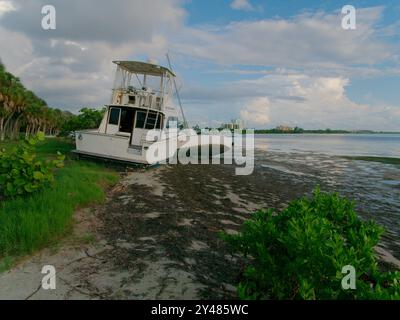 Weite Aussicht auf Ebbe-Pfützen in Richtung angespülltes, großes weißes Fischerboot am Maximo Park Water in Richtung Skyway Channel Stockfoto