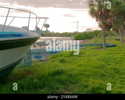 Weitwinkelblick über das Metallpontonrohr, das an Land in grünem Gras gespült wird, zum Krabbenanglerboot mit roten Schwimmbojen. Über Strand und Ebbe Stockfoto