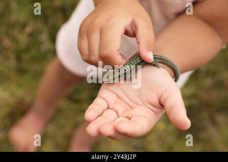 Kleines Mädchen mit Eidechse auf verschwommenem Hintergrund, Nahaufnahme. Kind genießt wunderschöne Natur Stockfoto