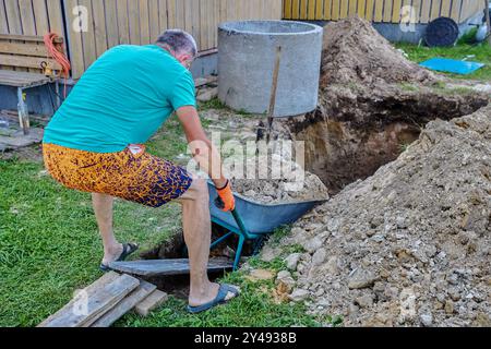 Hausbesitzer gräbt Grube, um Klärgrube aus Betonringen zu installieren. Stockfoto