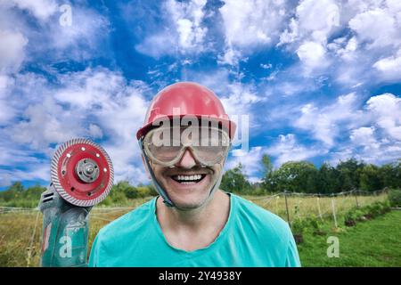 Rote Diamant-Kreissäge in den Händen eines verrückten Arbeiters mit wahnsinnigem Lächeln, mit Schutzbrille und Bauhelm. Stockfoto