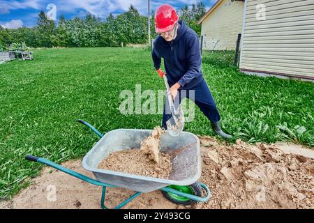 Arbeiter beladen Schubkarren mit Sand während der Bauarbeiten auf Vorortgelände. Stockfoto