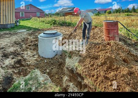 Der Baumeister füllt einen saugfähigen Graben in Abwasserleitungen mit Sand von Hand mit Bajonettschaufel. Stockfoto