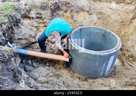 Einbau eines Einlassrohrs in das septische System aus Betonringen, Klempner markiert die Stelle für das Loch. Stockfoto