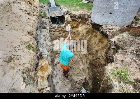 Beim Graben einer Grube für Klärgrube aus Betonringen verwendet der Hausbesitzer Bajonettschaufel und Gartenkarre. Stockfoto