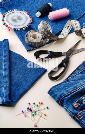 Nähzubehör und Denim-Stoff sind auf einem Arbeitsplatz angeordnet, um Kleidung in einem hellen Ambiente zu ändern Stockfoto