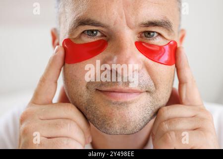 Mann, der Augenflecken auf das Gesicht aufträgt. Falten und Gesichtspflege zu Hause für Männer. Das Konzept der Gesichtsverjüngung Stockfoto