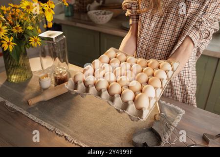 Ein Mann hält einen großen Eierkarton, in dem 30 Eier sichtbar sind. Im Hintergrund befindet sich eine Kücheneinrichtung mit Utensilien und Gläsern. Der Fokus liegt auf den Eiern in Stockfoto