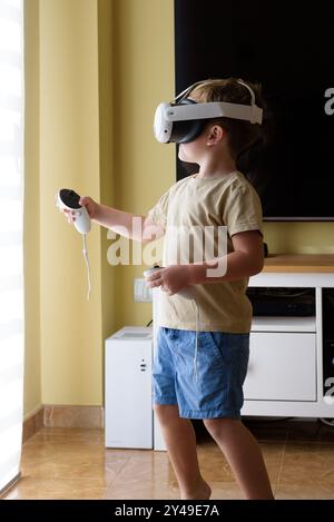 Begeistertes Kind mit einer Virtual-Reality-Brille im Wohnzimmer zu Hause. Schulbildungsprogramm für Kinder. Überraschter kleiner Junge, der mit VR gla aussieht Stockfoto