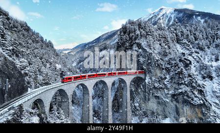 Schnee fällt und Zug fährt durch den berühmten Berg in Filisur, Schweiz. Express-Zug in den Schweizer Alpen im Schnee im Winter. Stockfoto