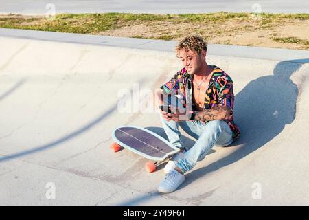 Ein Mann in einem bunten Hemd sitzt mit Skateboard Stockfoto