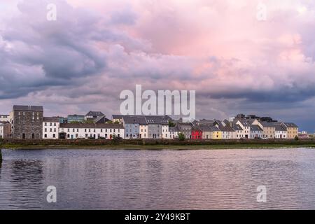 Am Ufer von Galway City, Irland, unter einem dramatischen Sonnenuntergangshimmel mit schweren Sturmwolken in sanften Rosa- und Grautönen, die sich auf dem ruhigen Flusswasser spiegeln Stockfoto