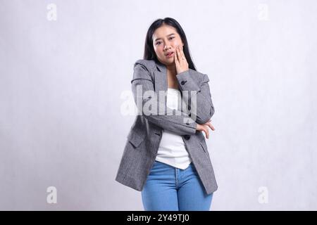 Geste der schönen erwachsenen Frau, die mit Zahnschmerzen zur Kamerahand klafft, die die Wange hält, die grauen Mantel und Jeans trägt, die isoliert auf weißem Hintergrund stehen. Stockfoto