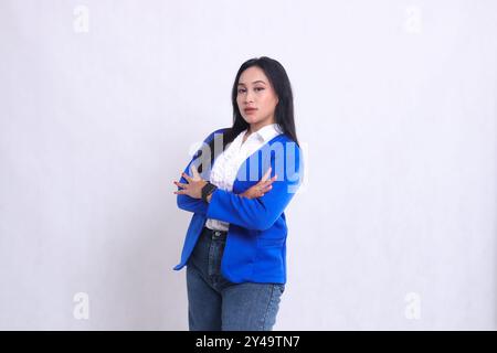 Der Charme einer schönen reiferen indonesischen Bürofrau, die eine formelle blaue Jacke trägt und in einem eleganten Winkel mit überkreuzten Armen steht. Für Unternehmen Stockfoto