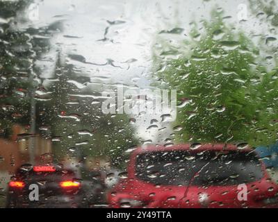 Eine enge Aufnahme eines regenbespritzten Fensters, die einen trafiktiven Autohintergrund enthüllt. Aus nächster Nähe Regentropfen am Fenster Stockfoto