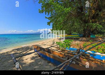 Outrigger-Kanus am weißen Sandstrand Pulisans mit Tangkoko Berg und Nationalpark dahinter. Pulisan, Minahasa Highlands, Nord-Sulawesi, Indonesien Stockfoto
