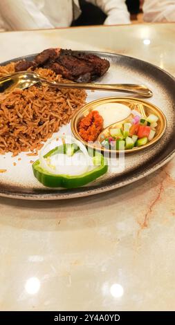 45 Grad Porträt von Nasi Kebuli (Kebuli-Reis) in der Mitte mit Gurken, Sauce und Löffel, typisch arabisches Essen hergestellt in Indonesien auf dem Tisch Closeu Stockfoto