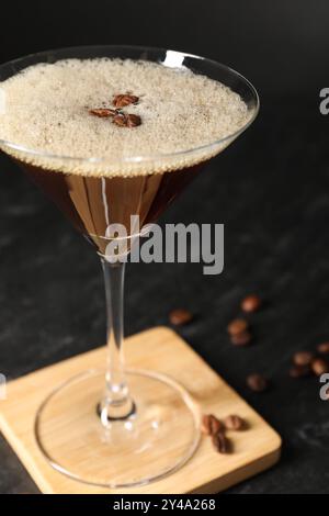 Ein Glas köstlicher Espresso-Martini und Kaffeebohnen auf einem dunklen, strukturierten Tisch, Nahaufnahme Stockfoto