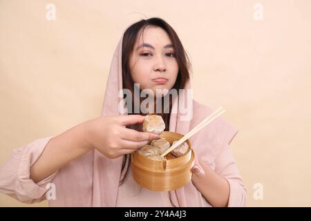 indonesien-Frau im Hijab, die Dimsum und eine Holzschale mit Essstäbchen und köstlichem Dimsum hält Stockfoto