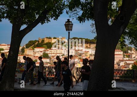 Ein Panoramablick bei Sonnenuntergang von Miradouro Sao Pedro de Alcantara auf eine dicht bebaute Stadtlandschaft, die vom Castelo de Sao Jorge auf einem Hügel hervorgehoben wird. Stockfoto