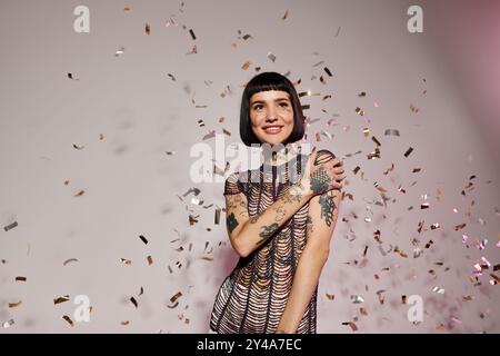 Eine stilvolle junge Frau lächelt hell, während sie von farbenfrohen Konfetti umgeben ist. Stockfoto