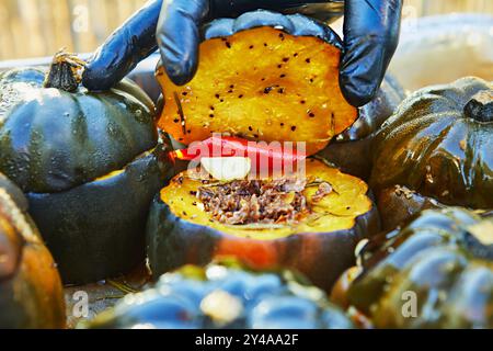 Nahaufnahme einer Hand mit Handschuhen, die einen gerösteten Kürbis aufhält, gefüllt mit geriebenem Rindfleisch, Knoblauch und rotem Pfeffer, bereit zum Servieren. Stockfoto