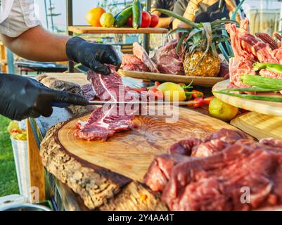 Eine Nahaufnahme eines Küchenchefs mit Handschuhen, der rohe Rindfleischstücke hält, sie auf einem Holzbrett zubereitete und Textur und Marmorierung zeigt. Stockfoto