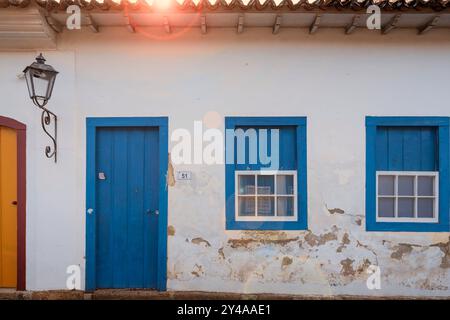 Paraty, Brasilien. Alte Hausfassade aus der Kolonialzeit. Holztüren und -Fenster mit blauer Farbe, Lampe und abblätternder Farbe. Streulicht. Stockfoto