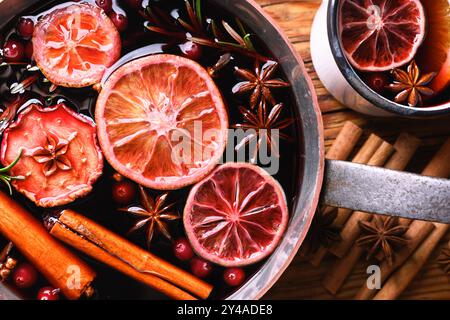 Nahaufnahme eines Kupfertopfes mit rotem Glühwein mit Scheiben von Orange, Apfel, Zimt, Sternanis, Rosmarin und Preiselbeeren. Lebensmittelfotografie Stockfoto