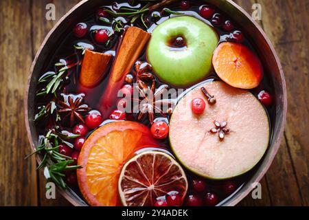 Nahaufnahme eines Kupfertopfes mit rotem Glühwein mit Scheiben von Orange, Apfel, Zimt, Sternanis, Rosmarin und Preiselbeeren. Lebensmittelfotografie Stockfoto