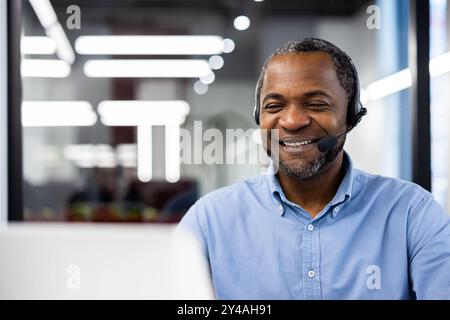 Selbstbewusster Afroamerikaner reifer Geschäftsmann in virtuellem Meeting. Lächelndes Headset für die Arbeit in modernen Büroumgebungen. Konzentrieren Sie sich auf professionelle Interaktion, Kommunikation und Technologie. Stockfoto