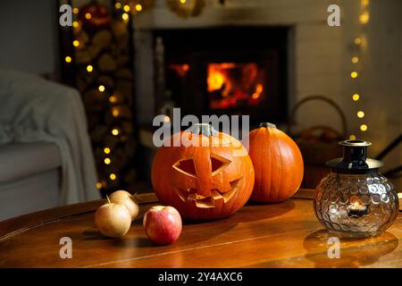 Halloween Kürbis Jack-o'-Laterne auf alten Holztisch mit brennendem Kamin Hintergrund in einem Wohnzimmer am Vorabend von Halloween, Feiertagsstimmung Stockfoto