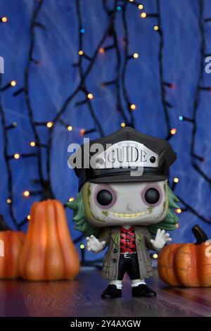 Funko Pop Actionfigur von BeetleJuice aus Tim Burton Comedy Horrorfilm. Blauer nebeliger Hintergrund, bunte Lichter, Halloween Kürbisse, Spinnennetz. Stockfoto