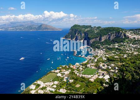 Blick aus der Vogelperspektive auf die atemberaubende Küste von Capri, Italien, mit den zerklüfteten Klippen, dem blauen Meer und dem geschäftigen Yachthafen mit Booten. Stockfoto